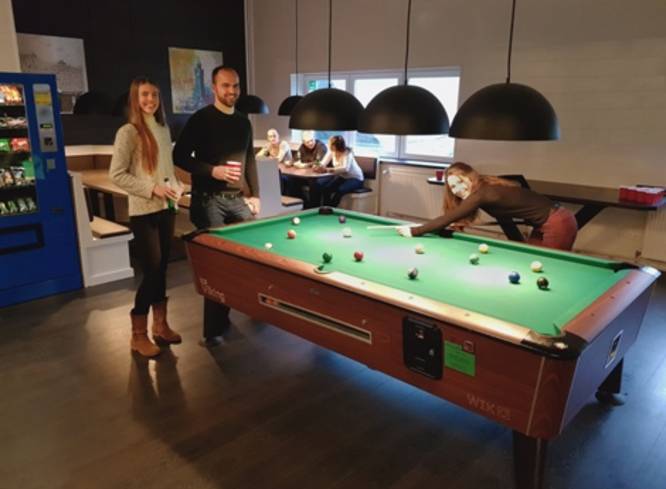 Gruppe spielt Billard, 2 Personen schauen zu.