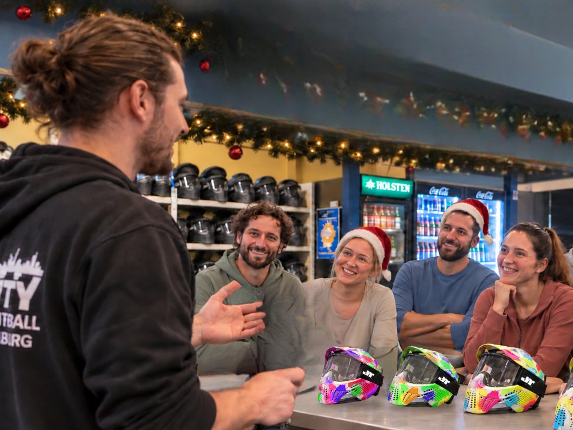 Betreuer erklärt einer Gruppe mit Weihnachtsmützen am Tresen von City Paintball Hamburg den Ablauf, vor ihnen stehen bunte Paintball-Masken