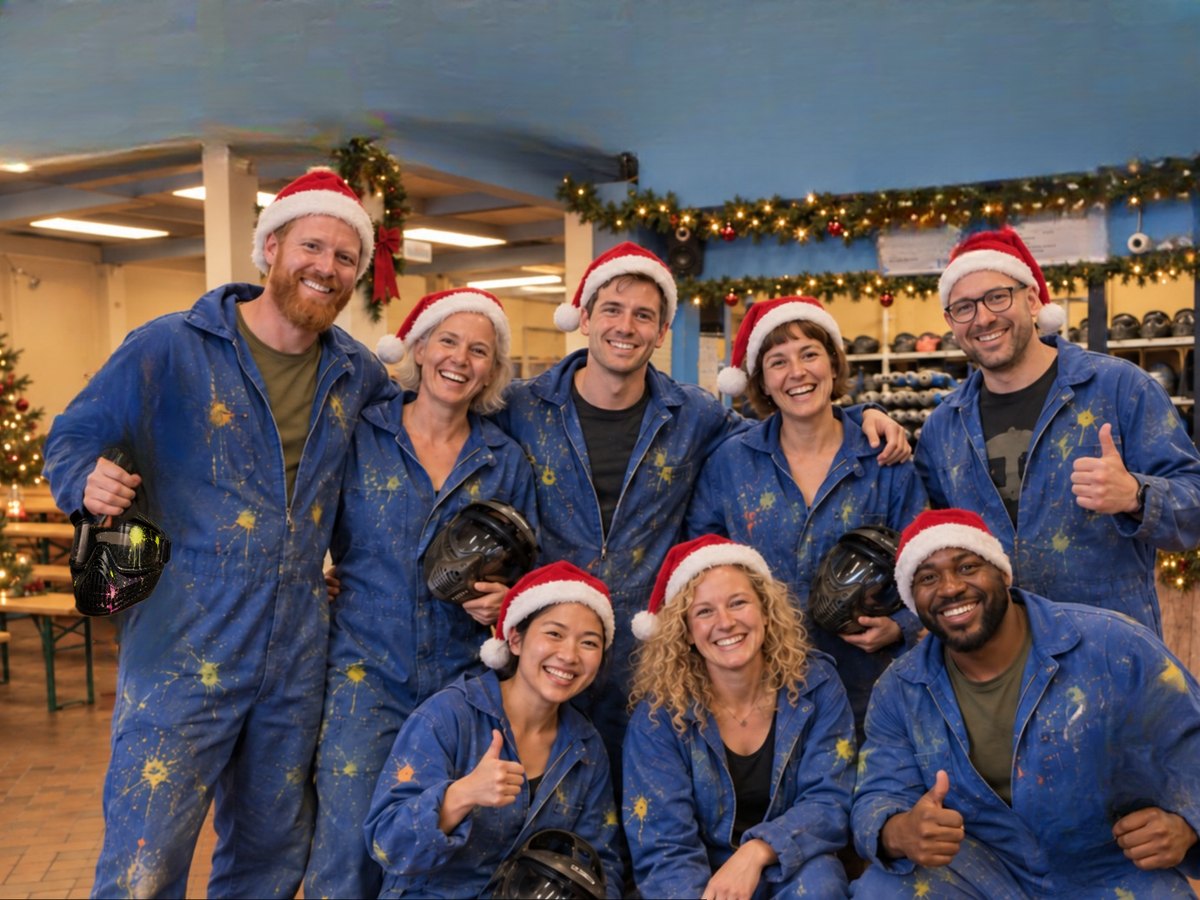 Fröhliches Team in farbbespritzten Overalls und Weihnachtsmützen mit Paintball-Masken bei City Paintball Hamburg